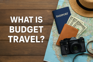 Travel essentials on a wooden table including a passport, map, wallet with dollar bills, camera, and straw hat — representing budget travel.