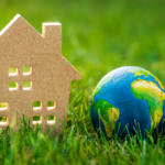 Cardboard house and Earth model on green grass symbolizing sustainable living and environmental harmony